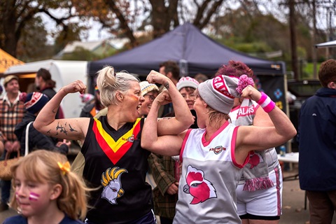Two women wearing AFL football jerseys flexing their biceps