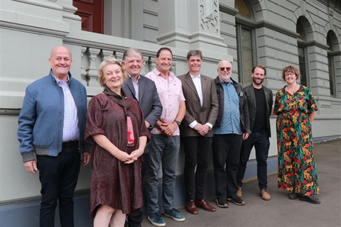 Eight people standing out the front of a building.